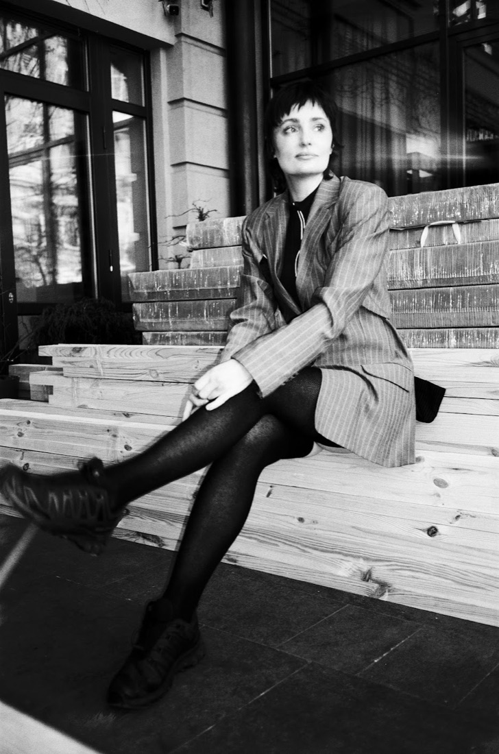 Oksana Hoshva sitting on wooden steps outside a building, black and white photo
